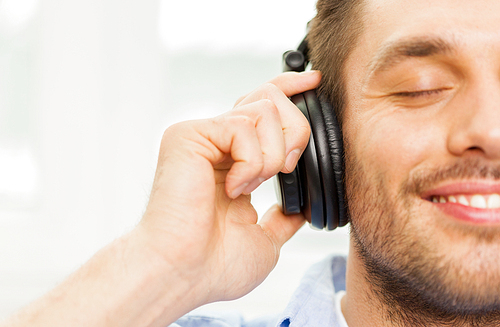 technology, music and people concept - smiling young man in headphones at home
