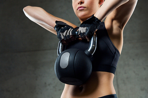 fitness, sport, exercising, weightlifting and people concept - close up of young woman flexing muscles with kettlebell in gym