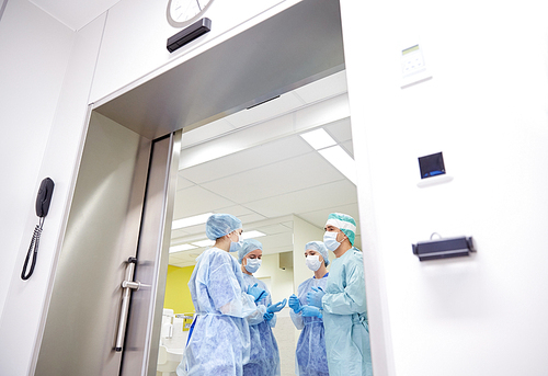 surgery, medicine and people concept - group of surgeons in operating room at hospital talking and preparing to operation