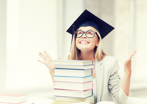 happy student in graduation cap with stack of books