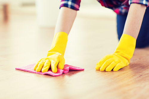 people, housework and housekeeping concept - close up of woman in rubber glover with cloth cleaning floor at home