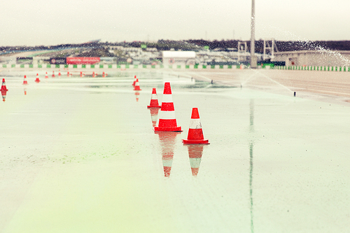 racing, motosports, extreme and motoring concept - traffic cones and sprinklers on wet speedway of stadium