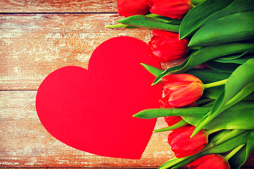 flowers, advertisement, valentines day and holidays concept - close up of red tulips and blank paper heart shape on wooden background