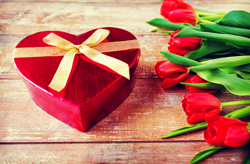 flowers, valentines day and holidays concept - close up of red tulips and heart shaped chocolate box on wooden table