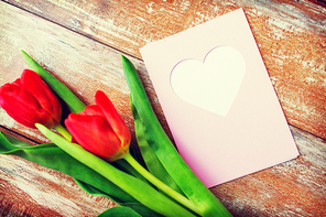 valentines day, greeting, love and holidays concept - close up of red tulips and greeting card with heart