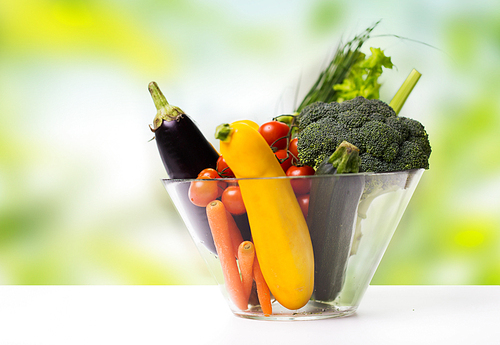 diet, vegetable food, healthy eating and objects concept - close up of ripe vegetables in glass bowl on table over green natural background