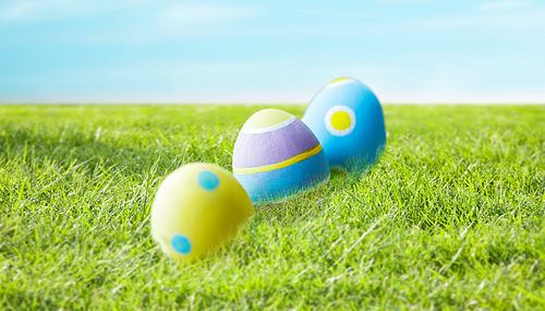 easter, holidays, tradition and object concept - close up of colored easter eggs and decorative grass on wooden surface over blue sky and grass background