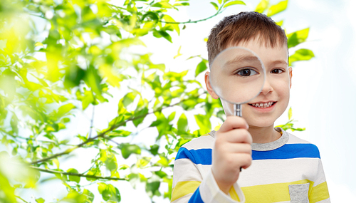 childhood, environment, ecology, discovery and people concept - happy little boy looking through magnifying glass over green natural background