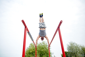 fitness, sport, training and lifestyle concept - young man exercising on parallel bars outdoors