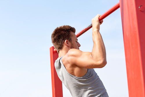 fitness, sport, exercising, training and lifestyle concept - young man doing pull ups on horizontal bar outdoors