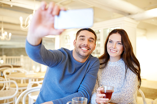 people, technology and dating concept - happy couple taking smartphone selfie and drinking tea at cafe or restaurant