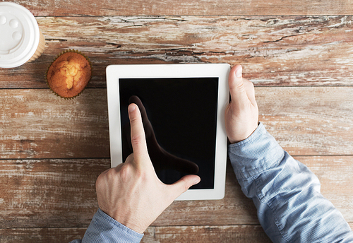 business, education, people and technology concept - close up of male hands with tablet pc computer, muffin and coffee cup on table