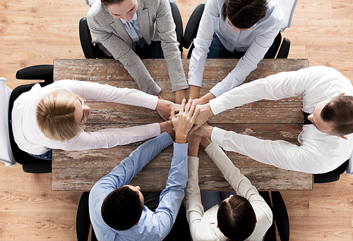 business, people, cooperation and team work concept - close up of creative team sitting at table and holding hands on top of each other in office
