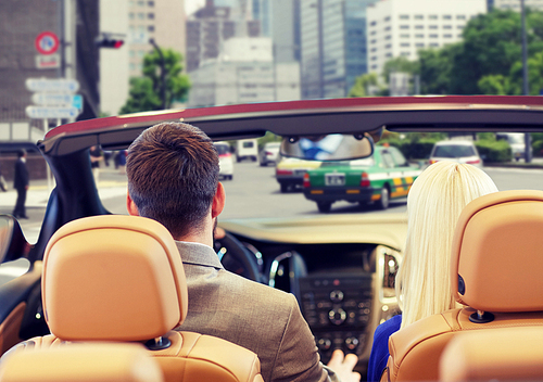 drive, auto transport and people concept - close up of couple driving in cabriolet car from back over city street background