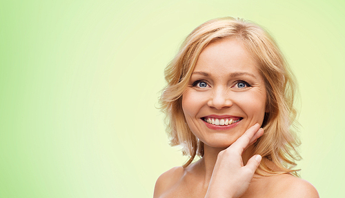 beauty, people and skincare concept - smiling woman with bare shoulders touching face over green natural background