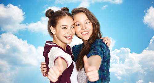 people, friends, teens and friendship concept - happy smiling pretty teenage girls hugging and showing thumbs up over blue sky and clouds background