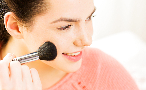 beauty, make up, cosmetics and people concept - close up of smiling young woman face applying blush with makeup brush