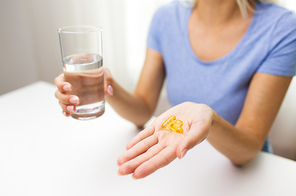 healthy eating, medicine, health care, food supplements and people concept - close up of woman hands holding pills or fish oil capsules and water glass at home