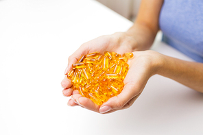 healthy eating, medicine, health care, food supplements and people concept - close up of woman hands holding pills or fish oil capsules at home