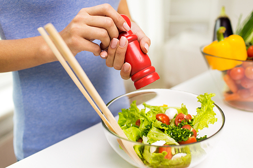 healthy eating, vegetarian food, cooking and people concept - close up of young woman seasoning vegetable salad with salt or pepper at home