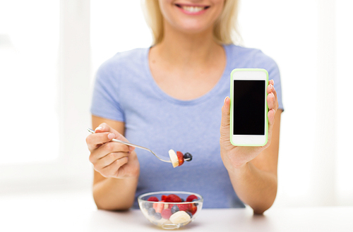 healthy eating, dieting, technology, food and people concept - close up of young woman with smartphone eating fruit salad at home