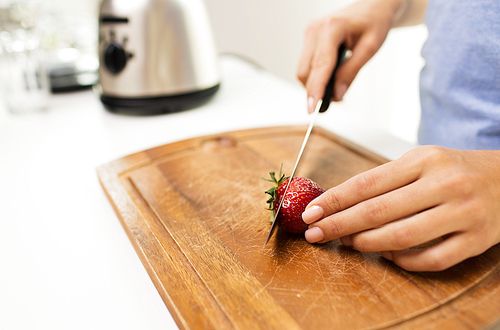 healthy eating, cooking, vegetarian food, weight lossing and people concept - close up of woman chopping strawberry at home