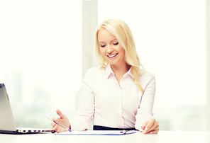 education, business and technology concept - smiling businesswoman or student with laptop computer and papers sitting in office