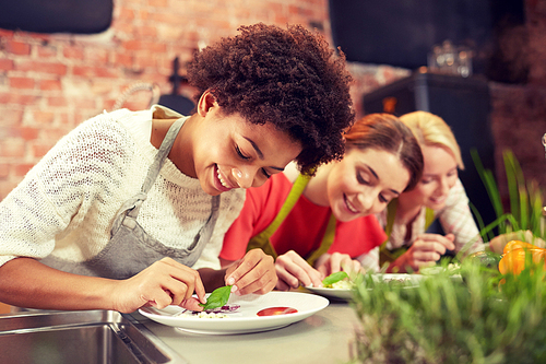 cooking class, friendship, food and people concept - happy women cooking and decorating plates with dishes in kitchen