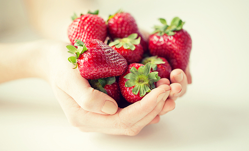 healthy eating, weight lossing, vegetarian food and people concept - close up of woman hands holding strawberries at home
