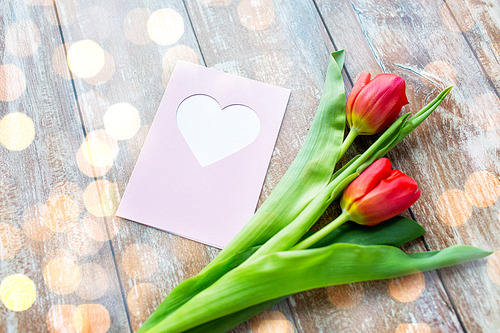 valentines day, greeting, love and holidays concept - close up of red tulips and greeting card with over lights