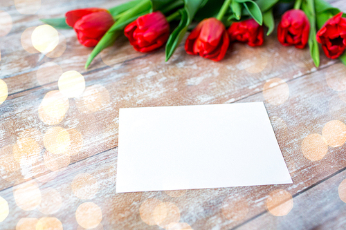 advertisement, valentines day, greeting and holidays concept - close up of red tulips and blank paper or letter on wooden background over lights