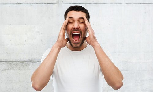 emotions, stress, madness and people concept - crazy shouting man in t-shirt over gray wall background
