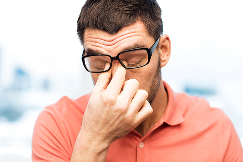 people, eyesight, stress, overwork and business concept - tired man in eyeglasses rubbing his eyes at home or work