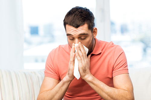 health care, flu, allergy, hygiene and people concept -sick man blowing nose to paper napkin at home