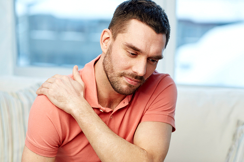 people, healthcare and problem concept - unhappy man suffering from neck or shoulder pain at home