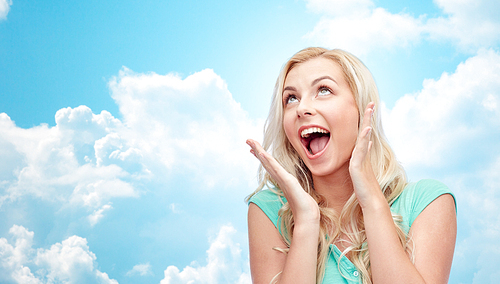 emotions, expressions and people concept - surprised smiling young woman or teenage girl over blue sky and clouds background