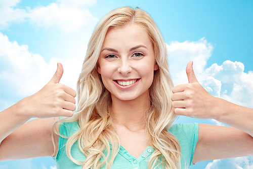 positive gesture and people concept - smiling young woman or teenage girl showing thumbs up with both hands over blue sky and clouds background