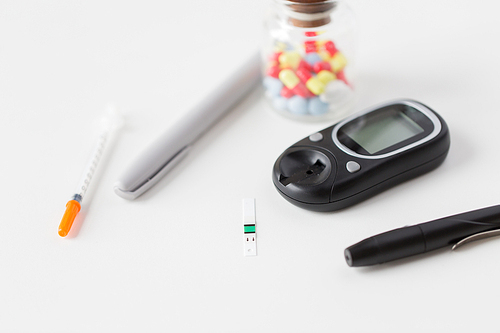 medicine, diabetes and health care concept - close up of blood sugar test stripe, glucometer, insulin pen and other diabetic tools on table