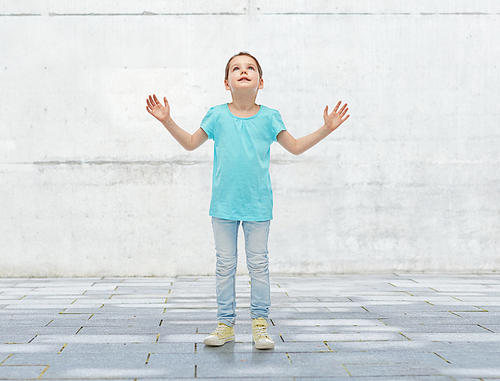 childhood, fashion, fun and people concept - happy little girl looking up to something over urban concrete background