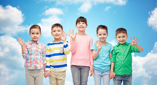 childhood, fashion, friendship and people concept - group of happy smiling little children holding hands over blue sky and clouds background