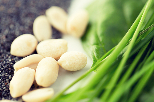 healthy eating, vegetarian food, culinary and diet concept - close up of peeled peanuts, greens and poppy or chia seeds