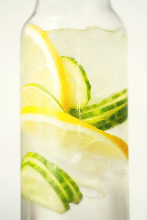 healthy eating, drinks,  and detox concept - close up of fruit water with lime, lemon and cucumber in glass bottle