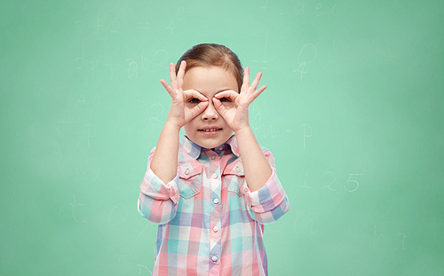 childhood, fun, school, education and people concept - happy little girl making faces over green chalk board background
