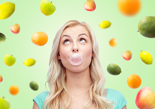 summer, healthy eating, emotions, expressions and people concept - happy young woman or teenage girl chewing gum over green background with fruits