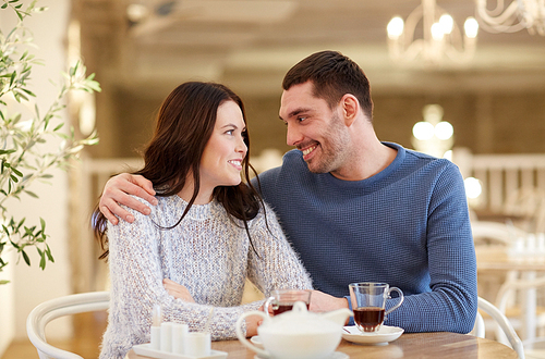 people, communication and dating concept - happy couple drinking tea and hugging at cafe or restaurant