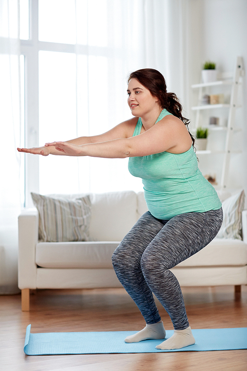 fitness, sport, exercising, training and lifestyle concept - smiling plus size woman doing squats on mat at home