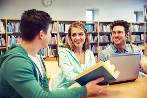 people, education, technology and school concept - happy students with laptop computer and book talking in library