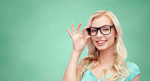 vision, education and people concept - happy smiling young woman or teenage girl glasses over green school chalk board background