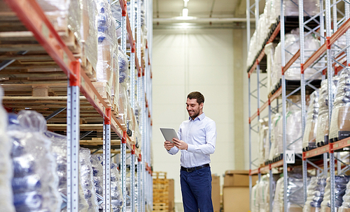 wholesale, logistic, business, export and people concept - happy man or manager with tablet pc computer checking goods at warehouse