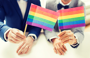 people, homosexuality, same-sex marriage and love concept - close up of happy male gay couple in suits and bow-ties with wedding rings holding rainbow flags